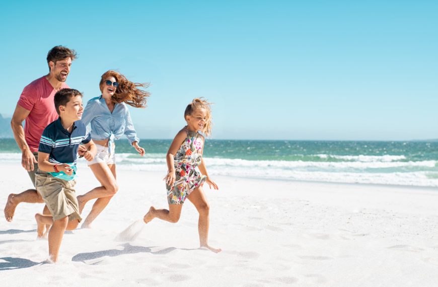Parents with children running on a beach while on vacation.
